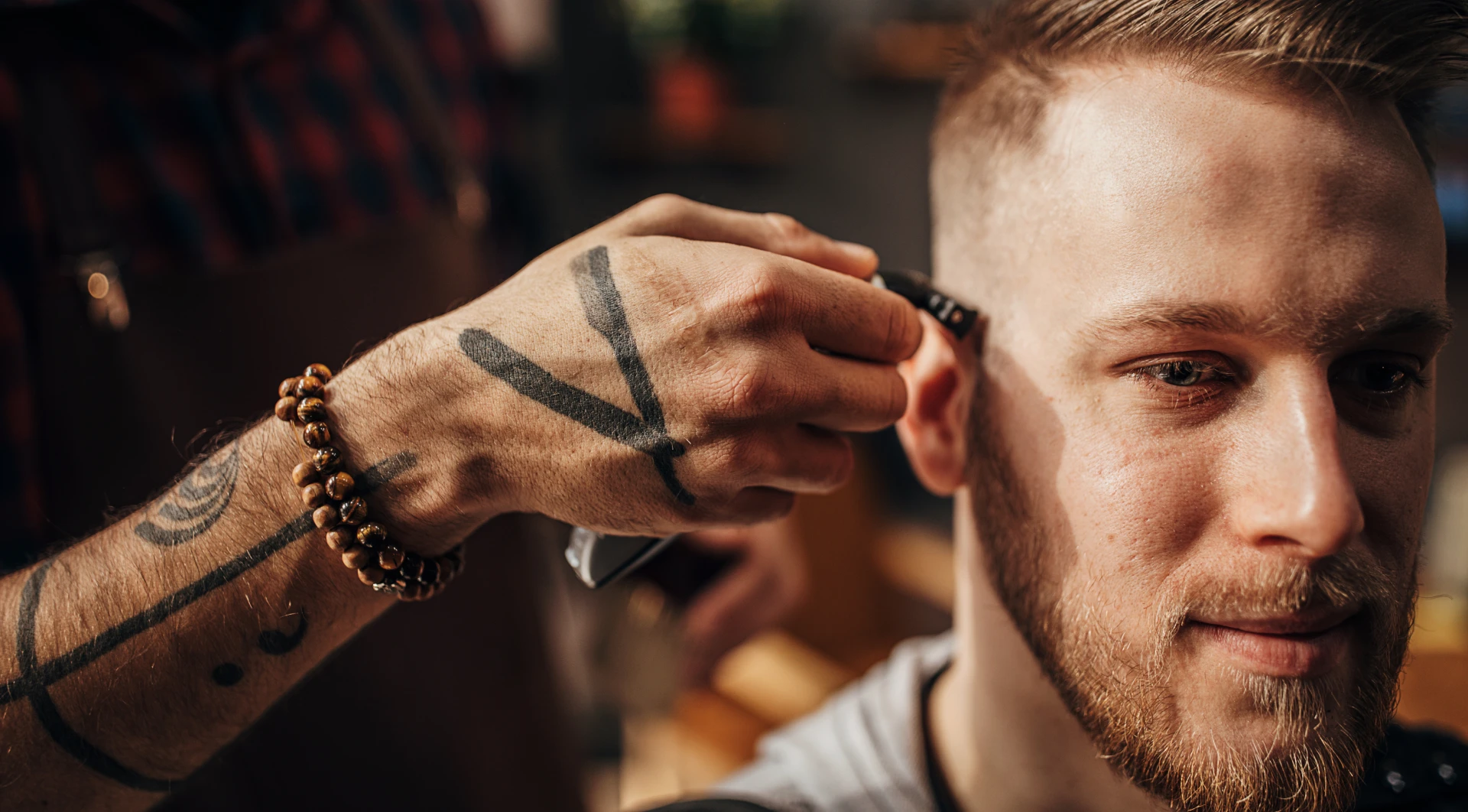 Man getting his hair cut by a barber, with a tattoo on his hand