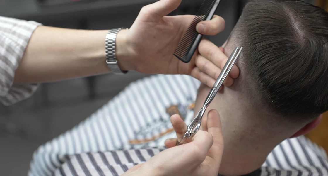 Man getting his hair cut by a barber, with the barber holding a pair of scissors